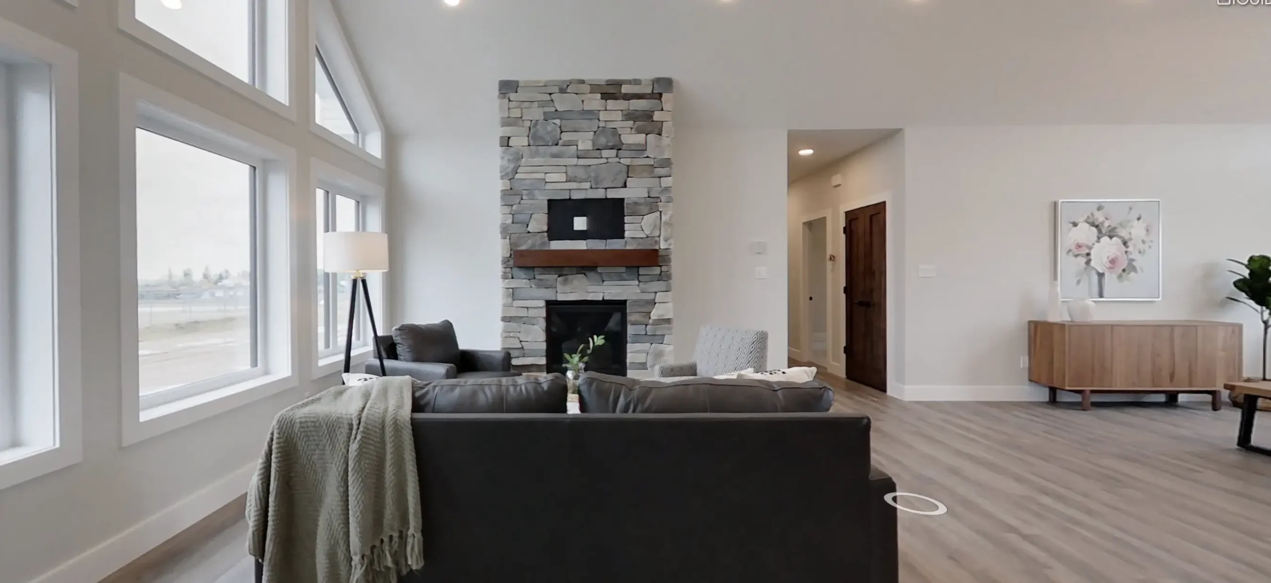 RTM home living room in Alberta or Saskatchewan with large grid windows, stacked stone fireplace with wood mantel, dark leather sofa, and light wood floors.